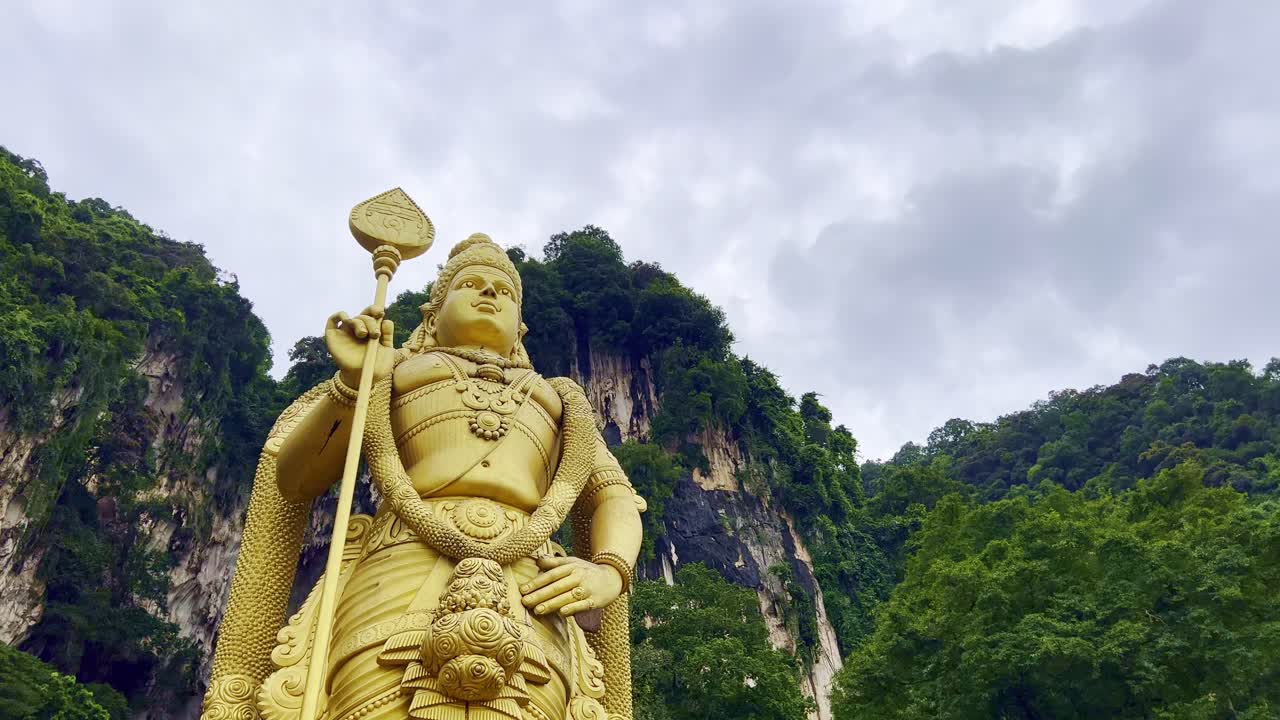 toma en ángulo bajo de la estatua dorada del dios hindú murugan frente al templo subramanya con la vista del acantilado montañoso en el fondo en malasia