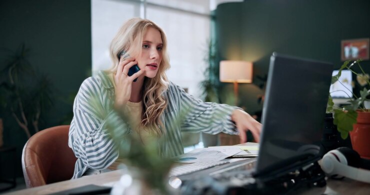 Giovane donna che lavora alla scrivania e parla al telefono in ufficio