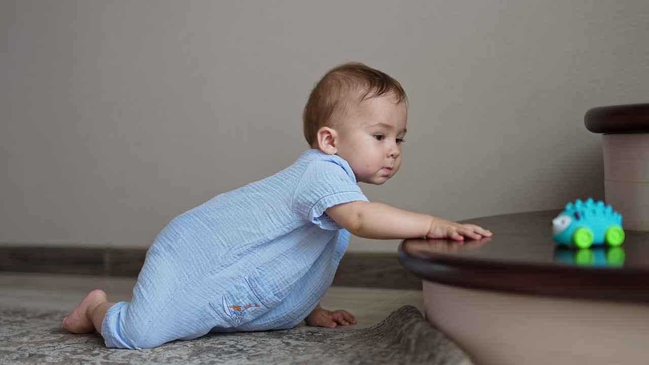 Cute adorable baby in blue romper crawls by the floor to the stairs. Beautiful child wants to get a toy from the stair.
