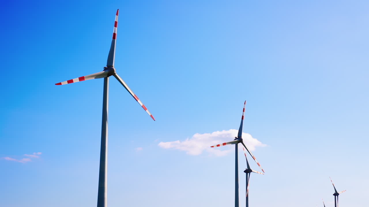 Wind turbines under a clear blue sky. Large wind turbines rotate slowly against a bright blue sky with a few clouds, highlighting renewable energy production