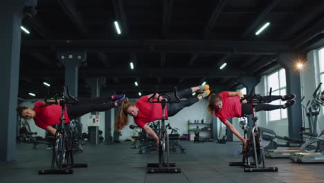 athletic women group training tricks on spinning stationary bike routine in gym, weight loss indoors