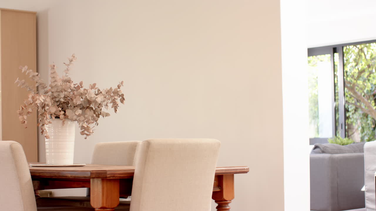 Dining table with vase of dried flowers and beige chairs in modern home, copy space