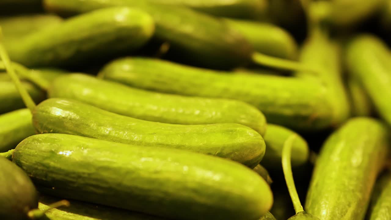 Close-up video of vibrant green cucumbers stacked in a market setting with warm lighting and a focused composition