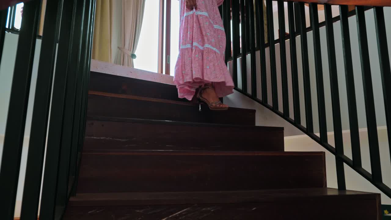 una chica desciende una escalera de madera en zapatos y un vestido largo rosa