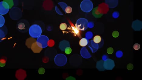Animation-of-sparkler-and-christmas-fairy-lights-flickering-over-black-background