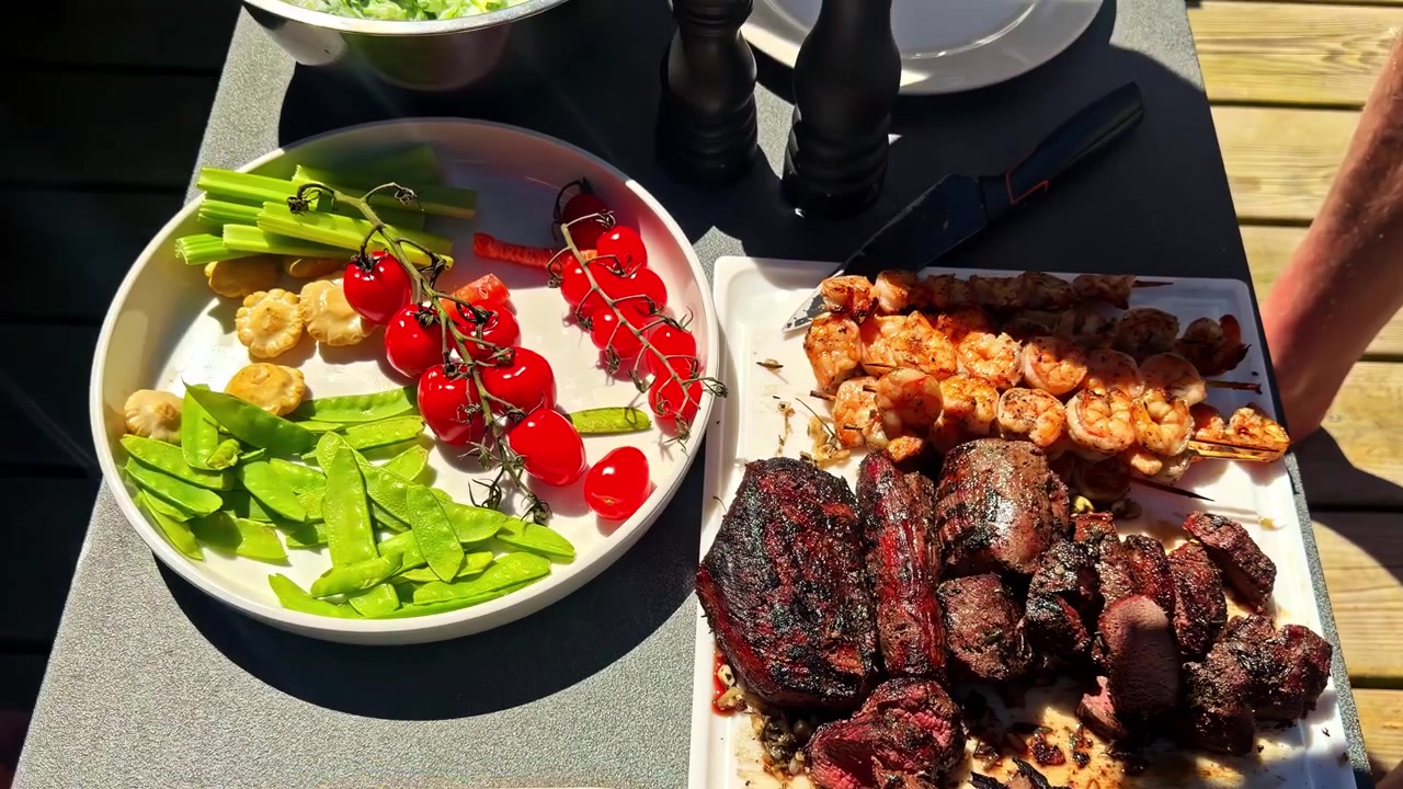 Různé grilované pokrmy a zelenina podávané venku během společného jídla, brambory, cuketa, čerstvá cherry rajčata a salát na piknik.