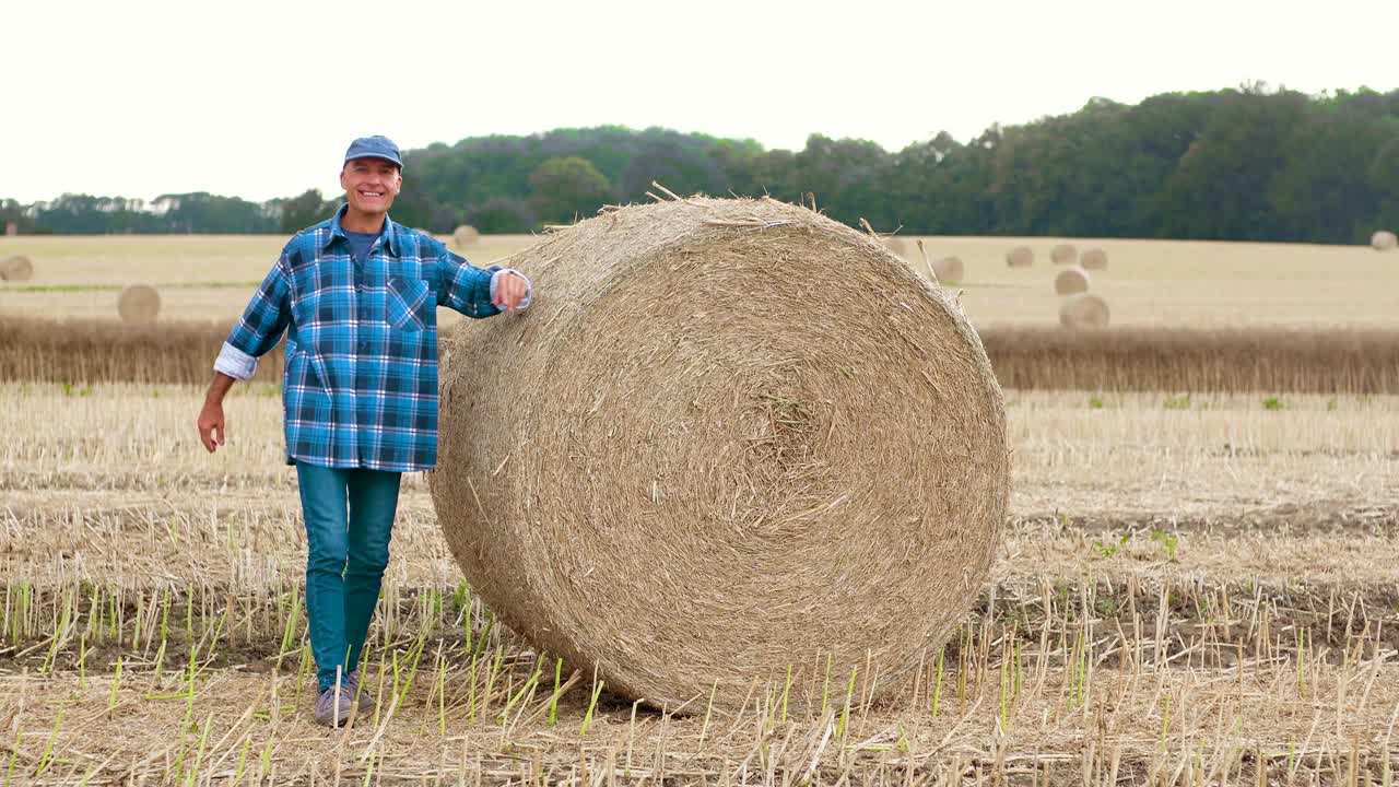 un granjero sonriente rodando balas de heno y gestando en la granja