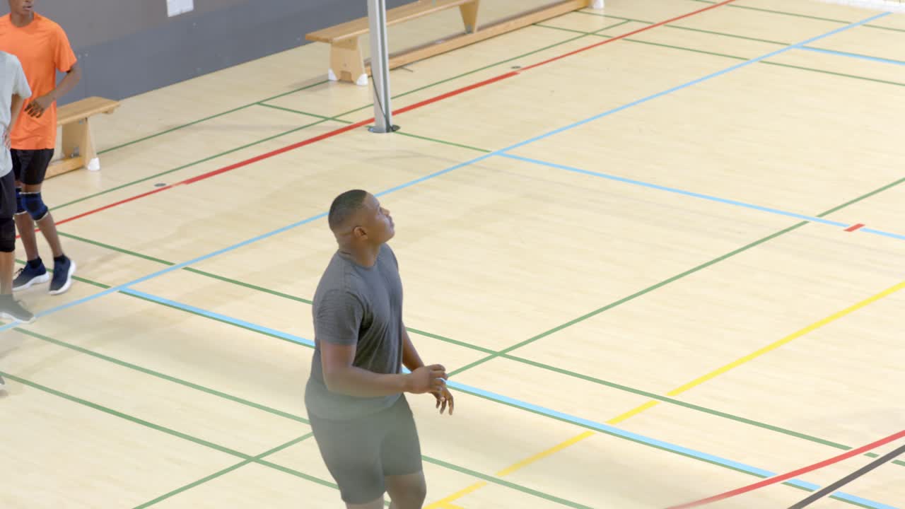 Coéquipiers masculins s'entraînant au contrôle du ballon dans un gymnase, après qu'un joueur en maillot rouge a lancé un volley-ball par-dessus le filet