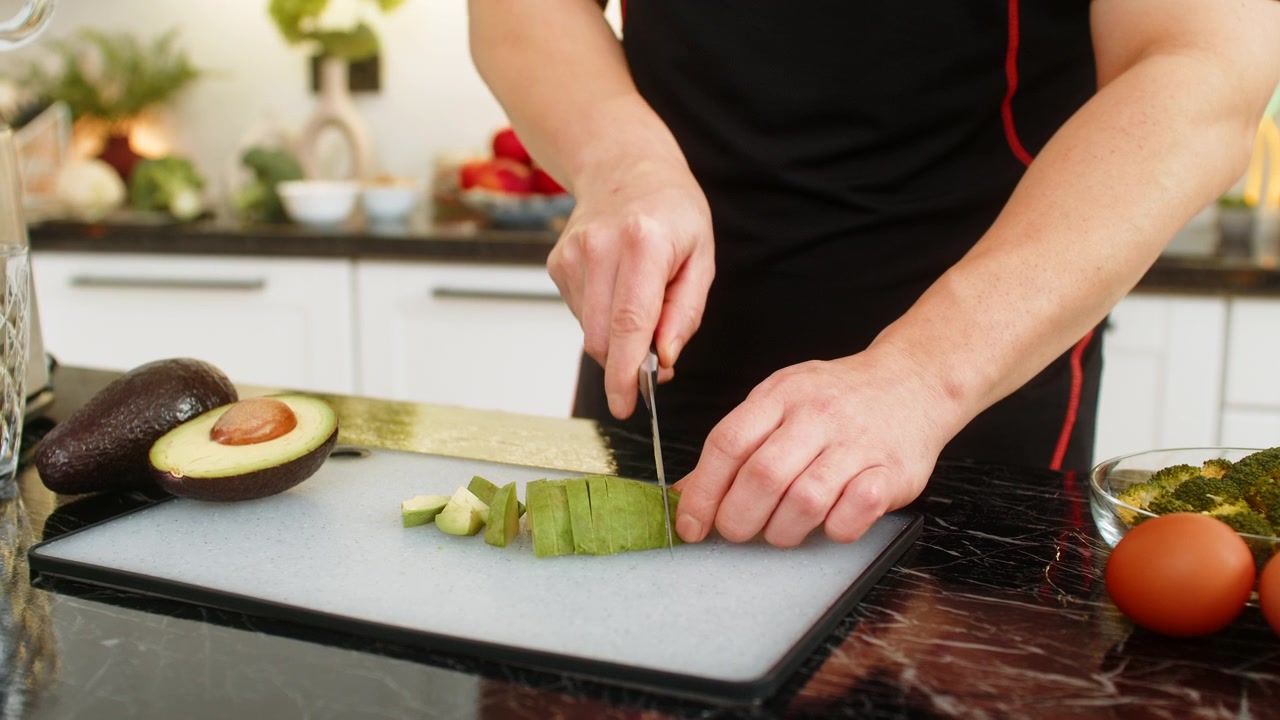 Uomo che taglia un avocado su un tagliere nella cucina di casa, mentre prepara un pasto sano ed equilibrato per una dieta depurativa