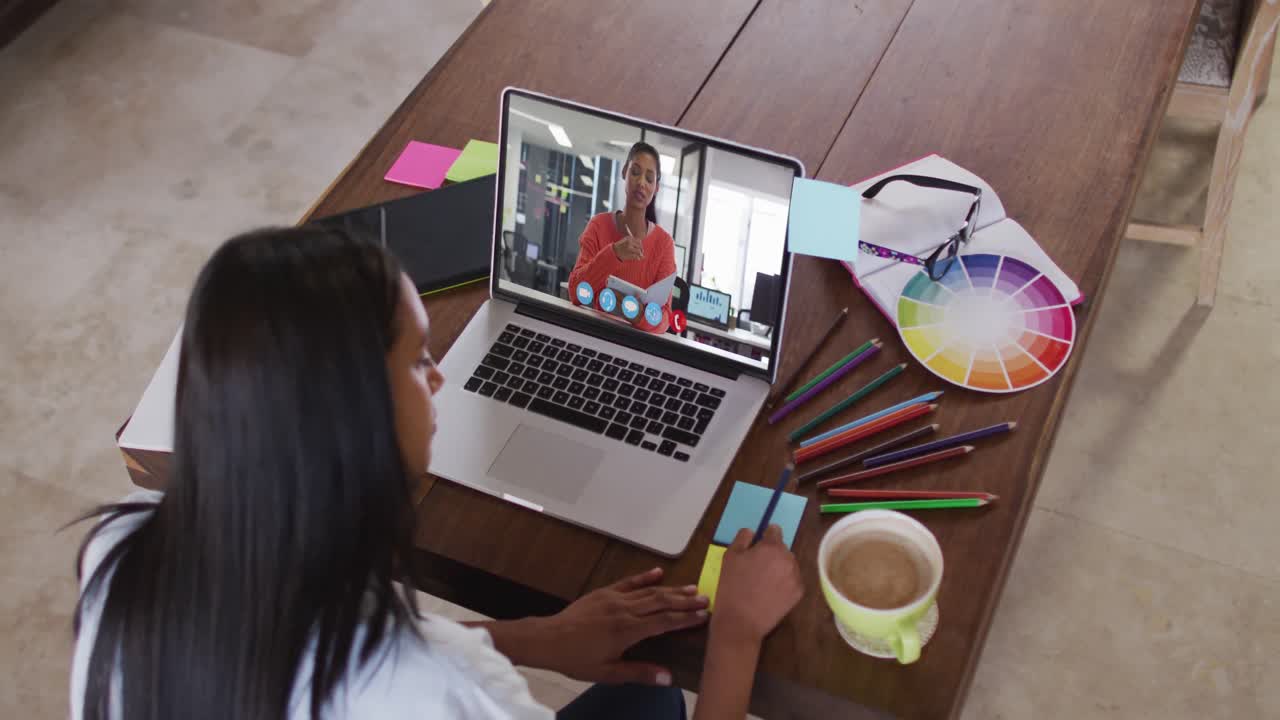 Empresaria mestiza sentada en una mesa usando el portátil haciendo una videollamada con una colega.
