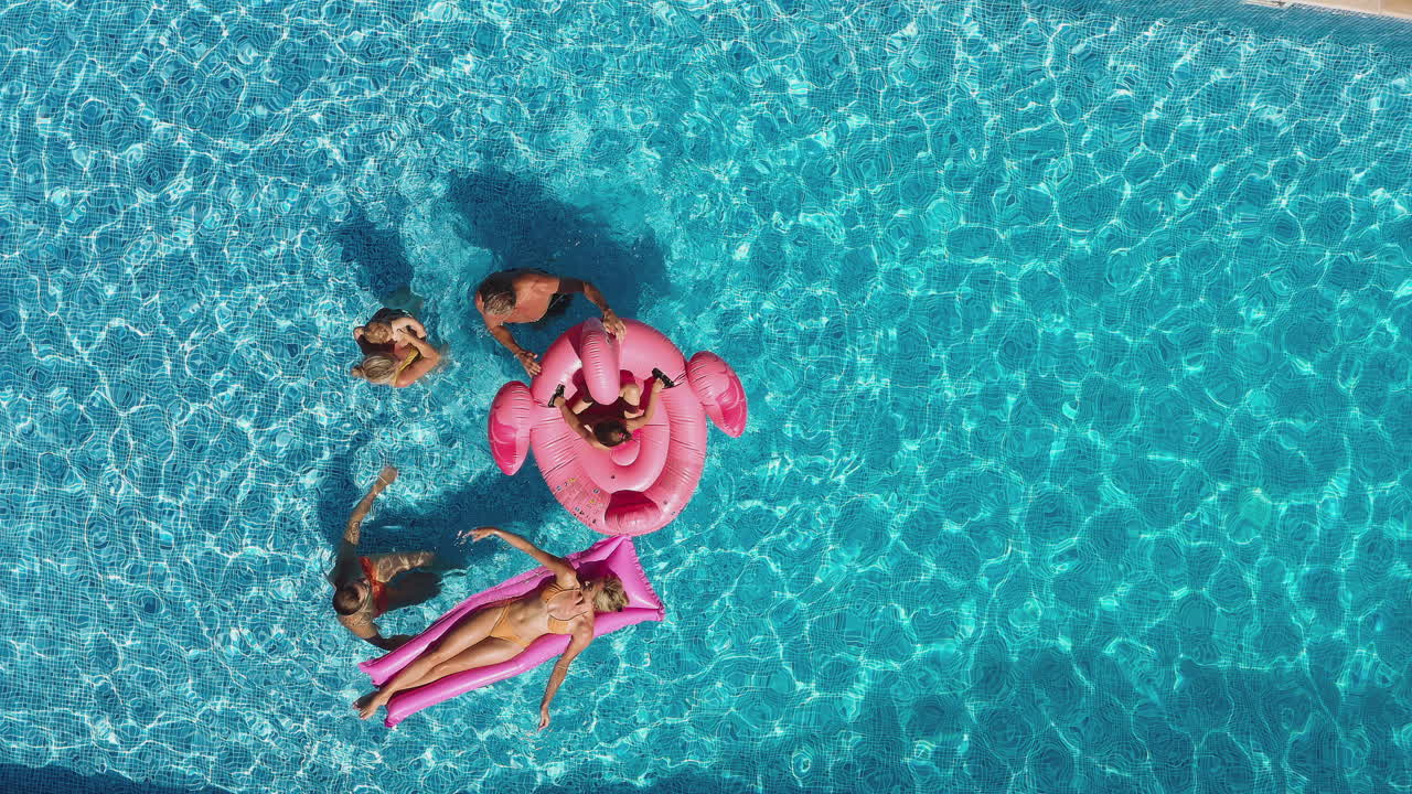 Overhead Drone Shot Of Multi-Generation Family With Inflatables On Summer Holiday In Swimming Pool