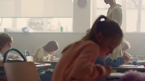 Children-doing-class-work-at-desks.-Teacher-explaining-lesson-to-pupils