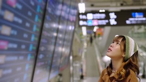 4k asian woman checking timetable flight schedule in airport terminal.