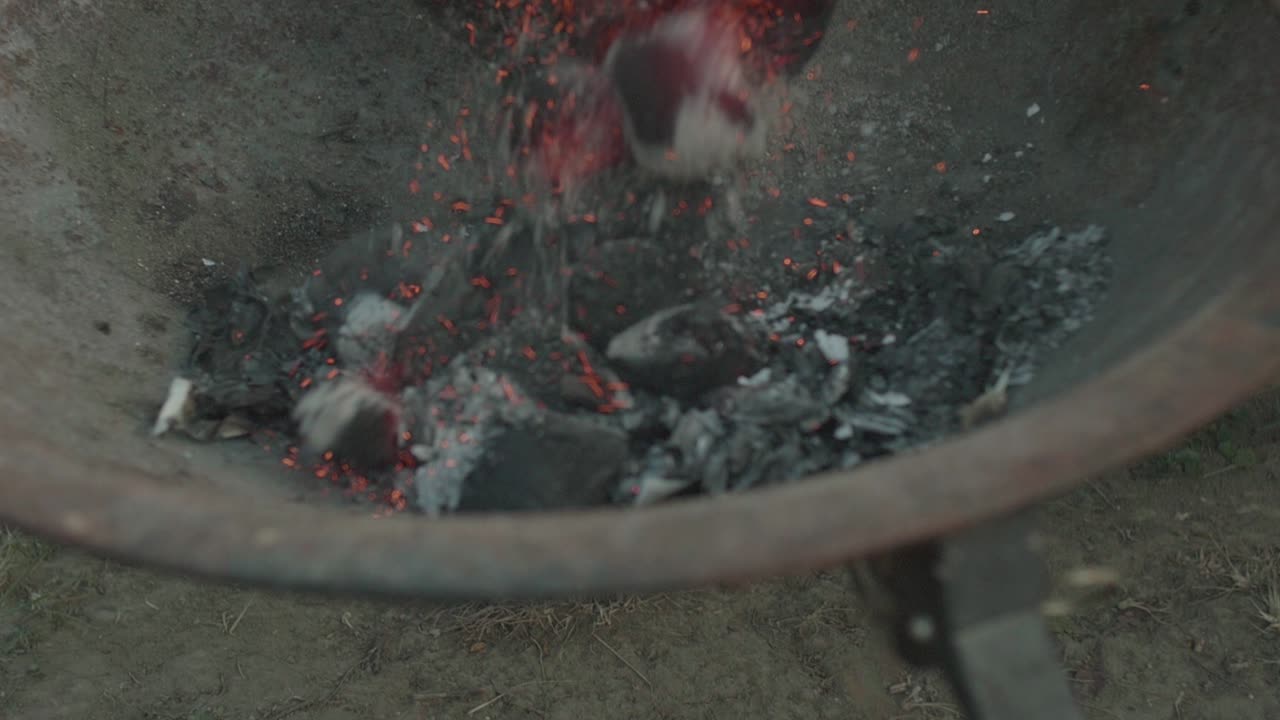 [CLOSE UP] of someone emptying a hot charcoal starter into a firebowl