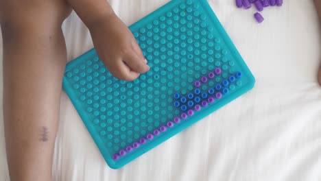 girl playing with colorful pegboard beads on her bed