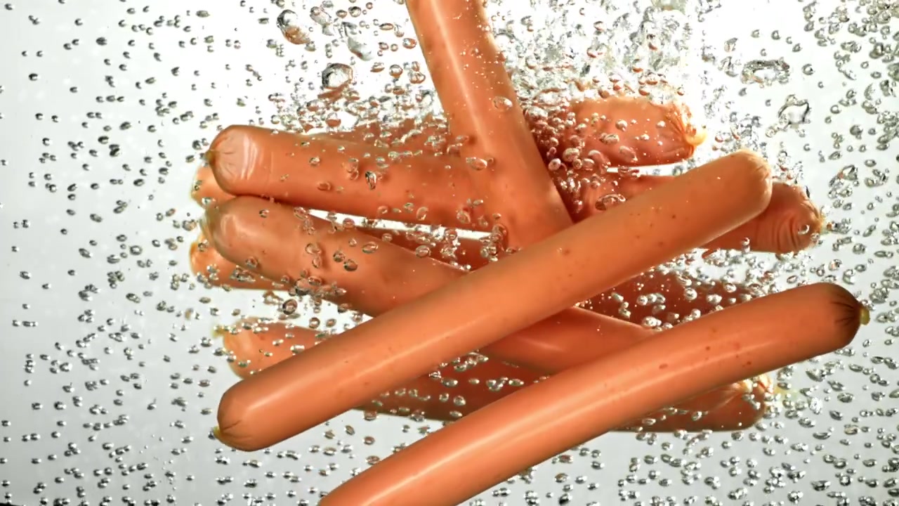 Salsicce che cadono in acqua bollente con bolle.