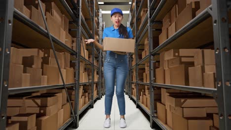 full body of asian female courier in blue uniform showing puzzled gesture and saying what while delivering a carton in warehouse