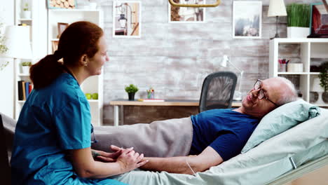 enfermera tomando un asiento cerca de un anciano enfermo que yace en una cama de hospital