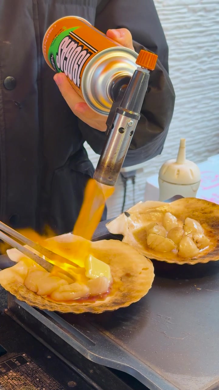 Close-up shot of a street food vendor blowtorching scallops with butter in their shells