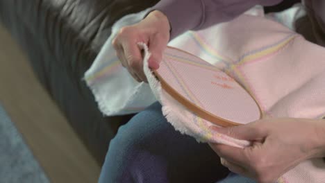 close-up shot of hands readjusting the wooden frame on a cross-stitch blanket