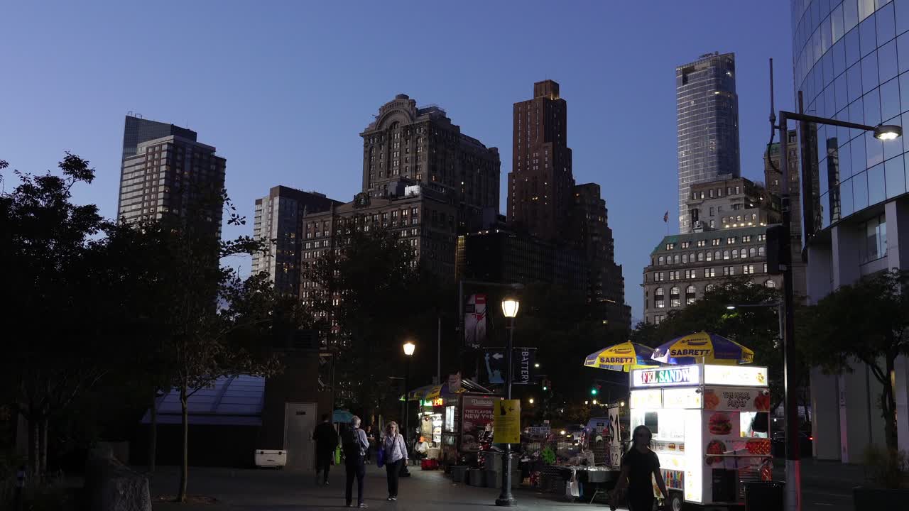 Wall Street at dusk, with quiet streets and a few pedestrians walking past the iconic buildings
