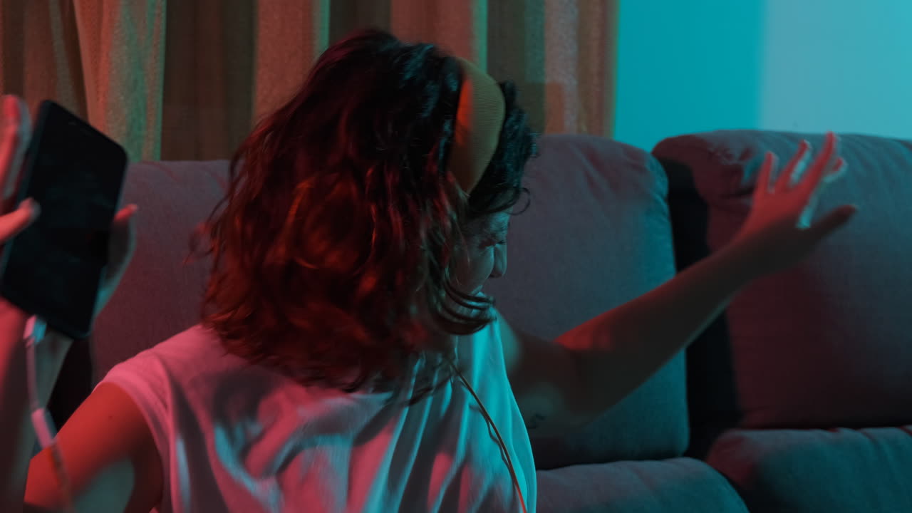 Young woman alone listening to music with headphones at home, colorful blue and red lights