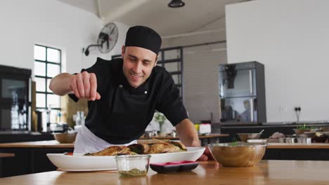 cocinero caucásico preparando un plato y sonriendo en una cocina