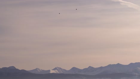 two hot air balloons flying high above snowy mountain landscape at sunset