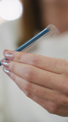 primer plano de manos con uñas pintadas examinando cuidadosamente una paja envuelta en plástico transparente, en un entorno interior moderno con iluminación suave y un fondo vibrante borroso