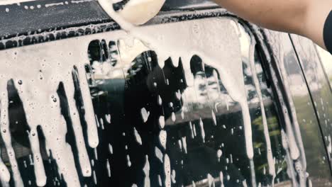 close up of a male washing a car wearing a black gloves with shampoo and sponge