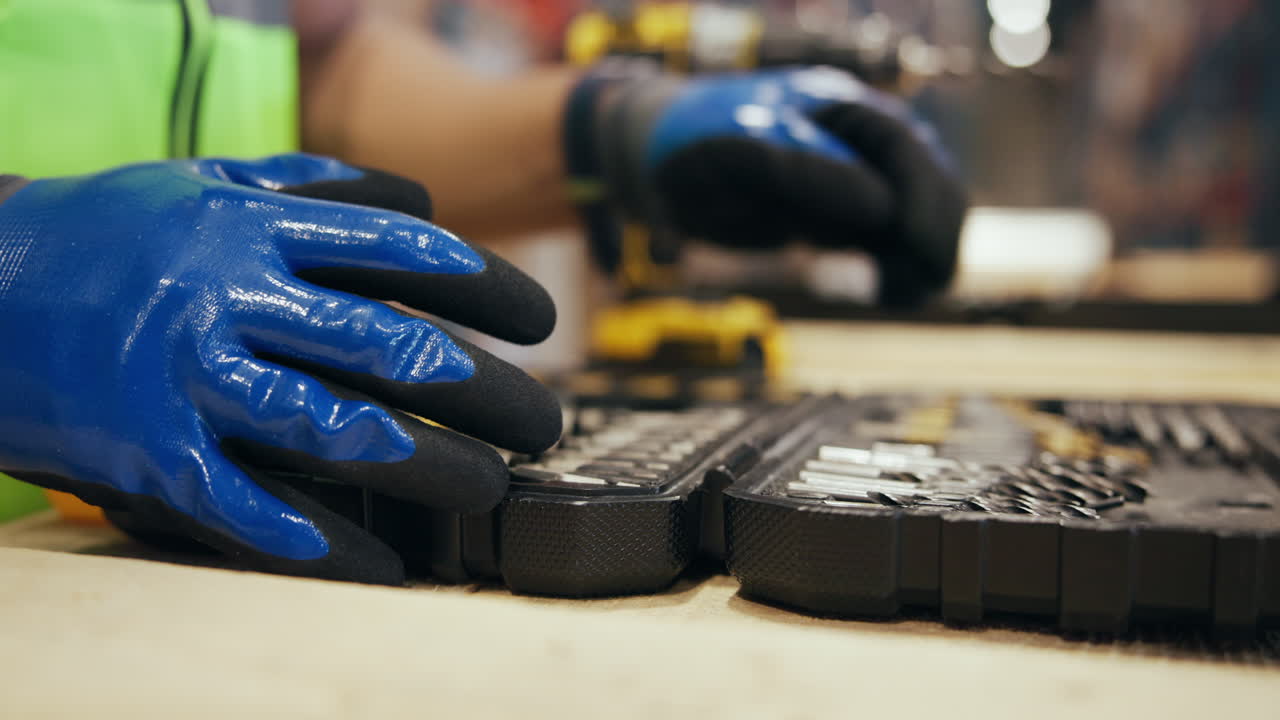 Trabajador con guantes azules abre una caja de herramientas y selecciona una broca