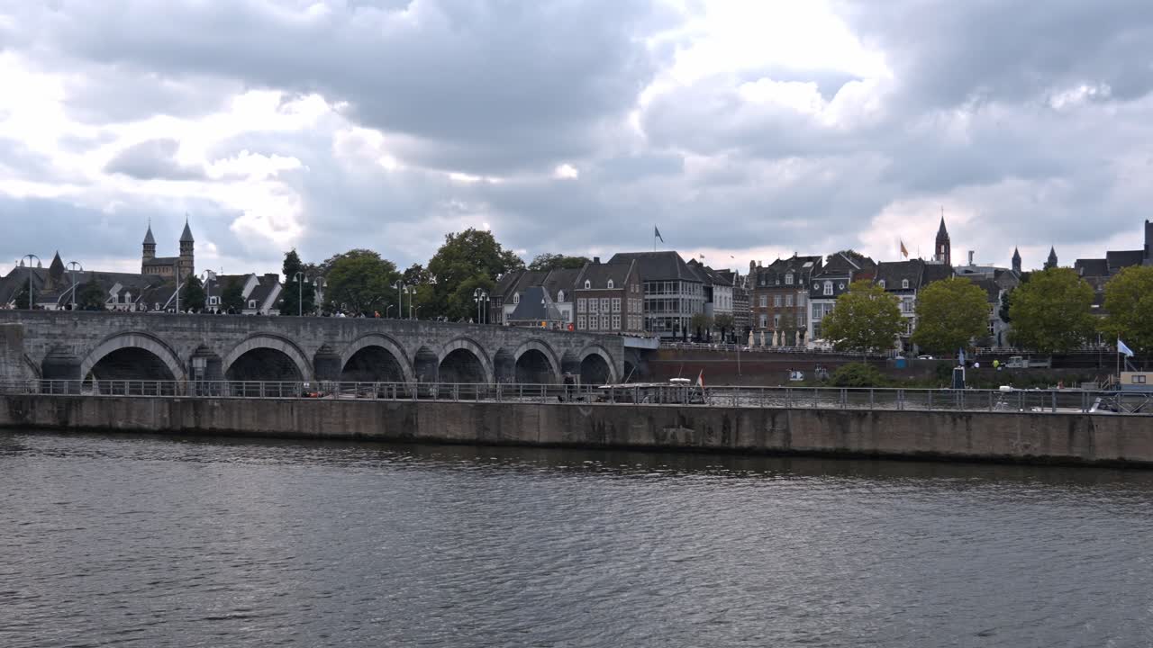 The Sint Servaasbrug (St. Servatius Bridge) spanning the Meuse River in Maastricht, Netherlands, under a dramatic, cloudy sky sunset