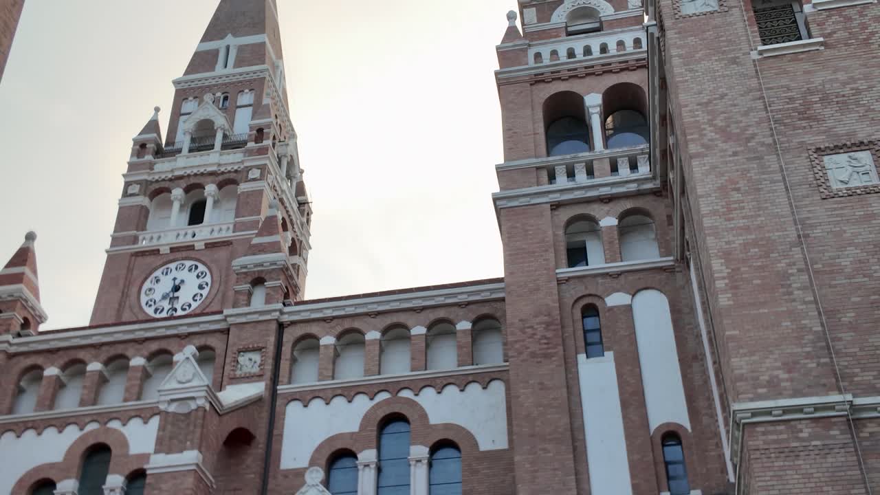Upward view of the Votive Church in Szeged, focusing on the clock tower and its elegant design