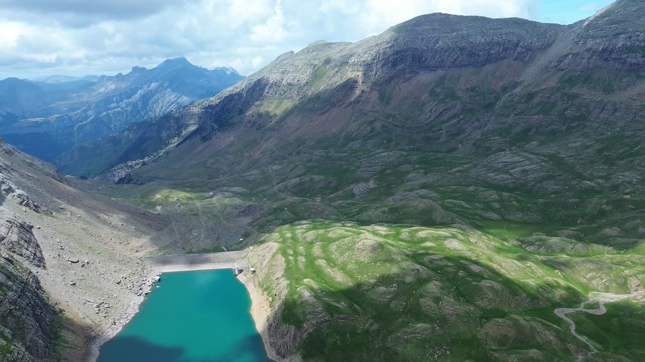 Drone zoom in toward the turquoise lake nestled among mountains in Valle de Ip, Aragón, with shadows over the terrain