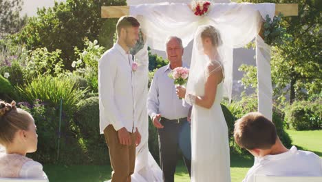Caucasian-bride-and-groom-standing-at-outdoor-altar-with-wedding-officiant-during-ceremony