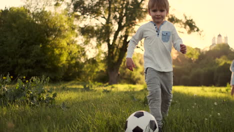 Glücklicher-Junge,-Der-Bei-Sonnenuntergang-Mit-Einem-Fußball-Auf-Einer-Sommerwiese-Läuft.