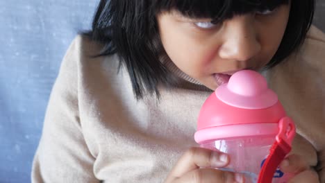 young girl drinking water from a pink bottle