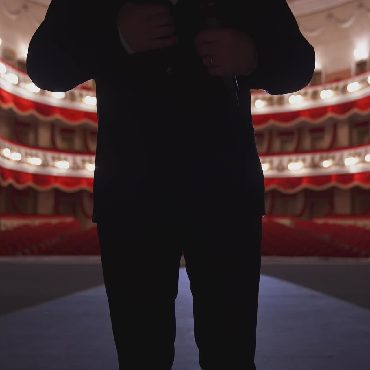 Unrecognizable man in suit on stage. Silhouette of a singer man holding a microphone on the background of empty theater hall.