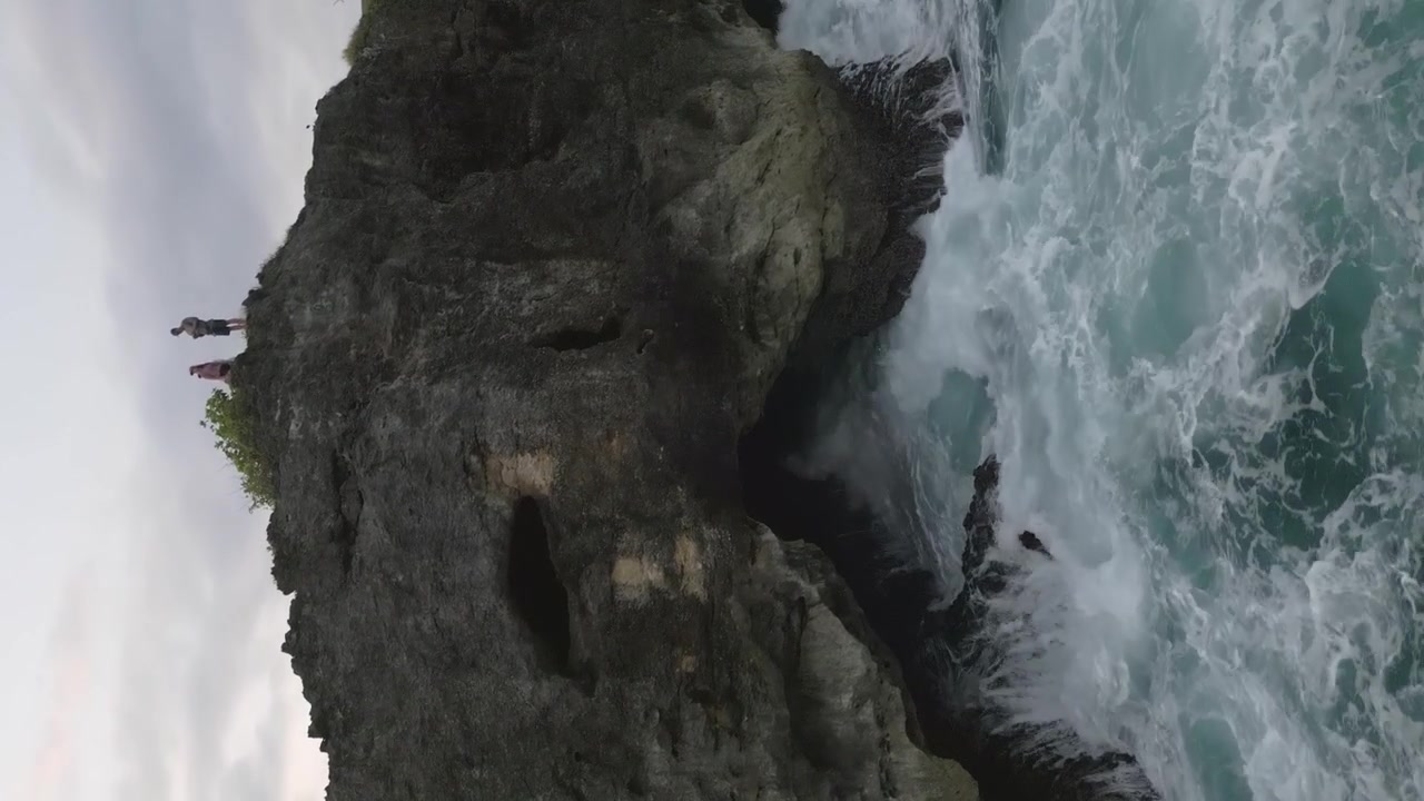 Turisti osservano dall'alto: le onde si infrangono violentemente contro la grotta di una scogliera marina, Bali