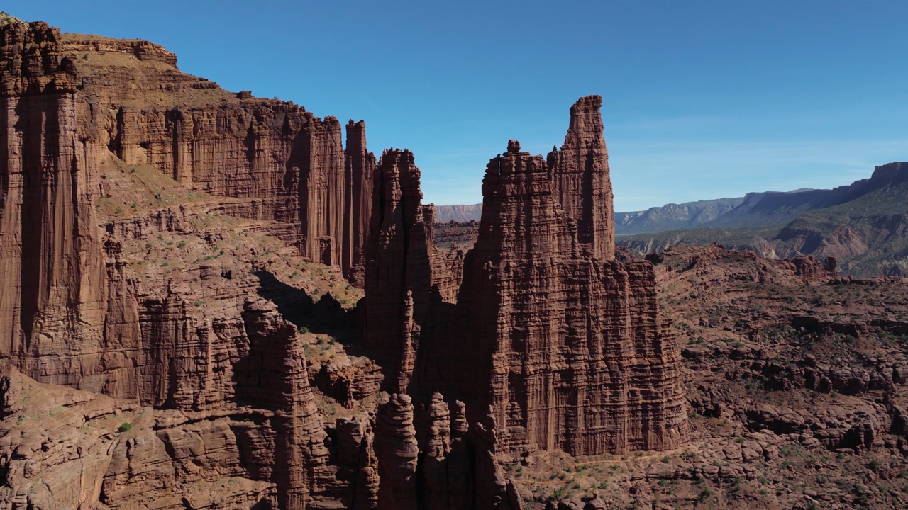 Fisher Towers sandstone rock formations rising from the desert landscape under a clear blue sky. Aerial, Push Forward Shot