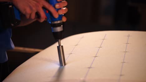 person drilling holes in a surfboard foam blank