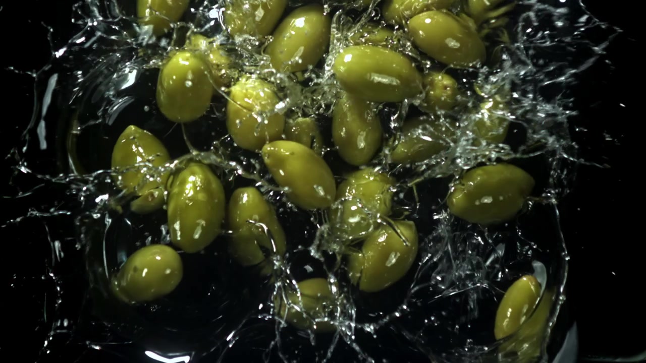 Olive verdi che cadono e schizzano nell'acqua su sfondo nero