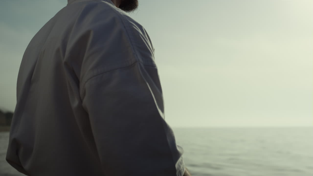 알려지지 않은 카라테 남자 손이 해가 지는 해변에서 전투 연습을 하고 있습니다.