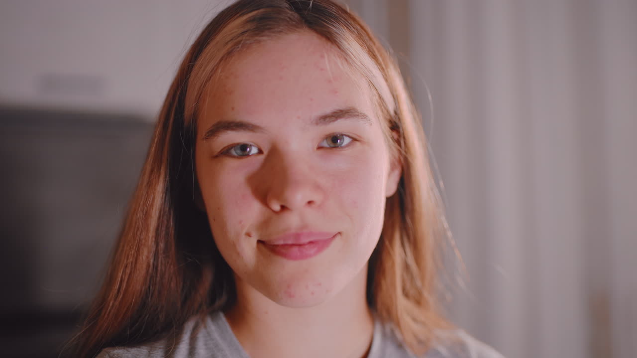 Close up of young woman with confident expression standing indoors, face softly lit in natural light, showing strength and calmness with subtle smile reflecting self assurance and natural beauty