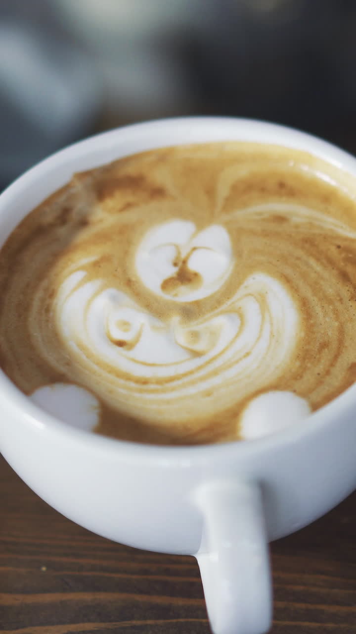 Hands of a bartender drawing with stick in a white cup of cappuccino. Process of making nice morning cappuccino coffee. Vertical video.