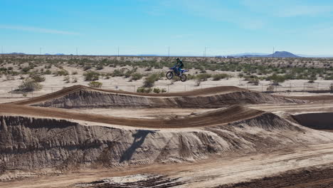 Off-road-motorcycle-taking-a-long-jump-off-a-dirt-ramp---slow-motion-sliding-aerial-view
