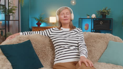 mature woman relaxing resting with calm music sitting on sofa with headphones eyes closed at home