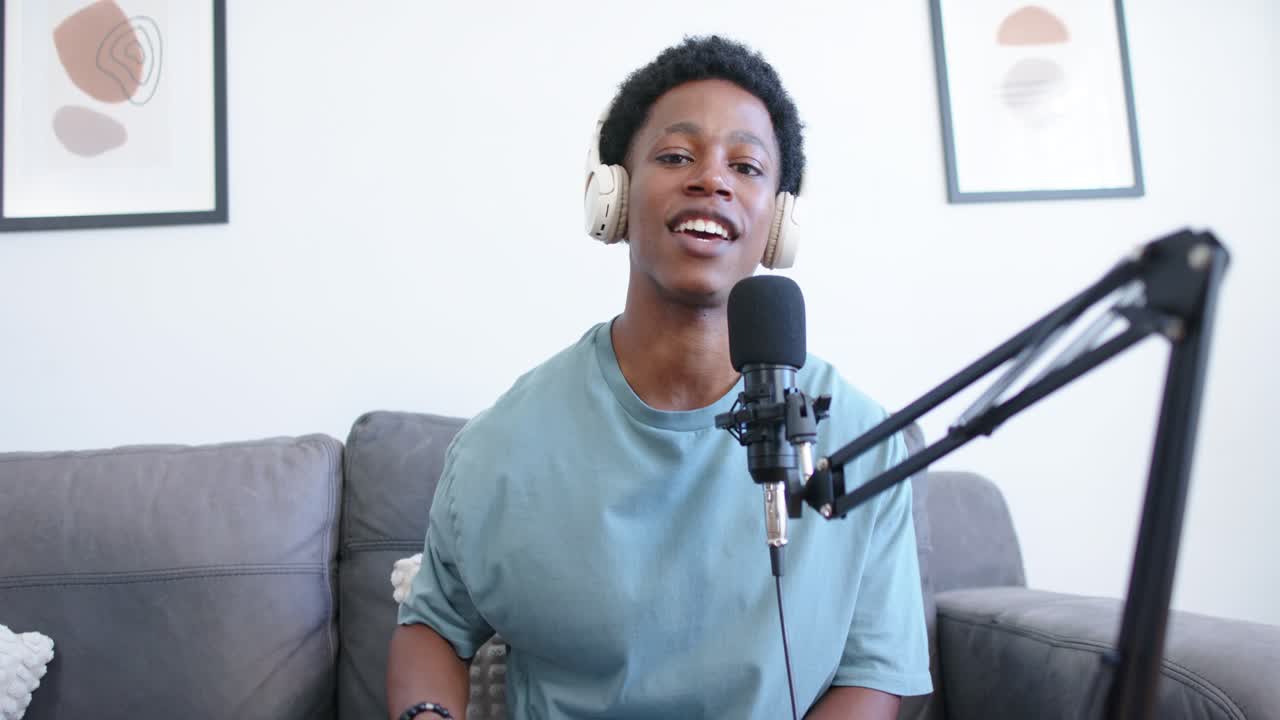 Podcastvært starter optagelse og taler ind i mikrofon på sofaen, gestikulerer mens han/hun henvender sig til publikum.