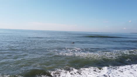 surfers taking a wild wave in high tide east bali indonesia dirty water, ketewel beach, 60 fps near the black stones, clear blue sky