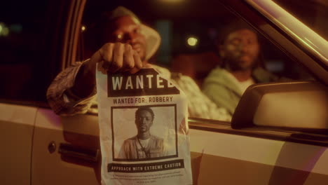 african american man showing wanted poster with his photo from car